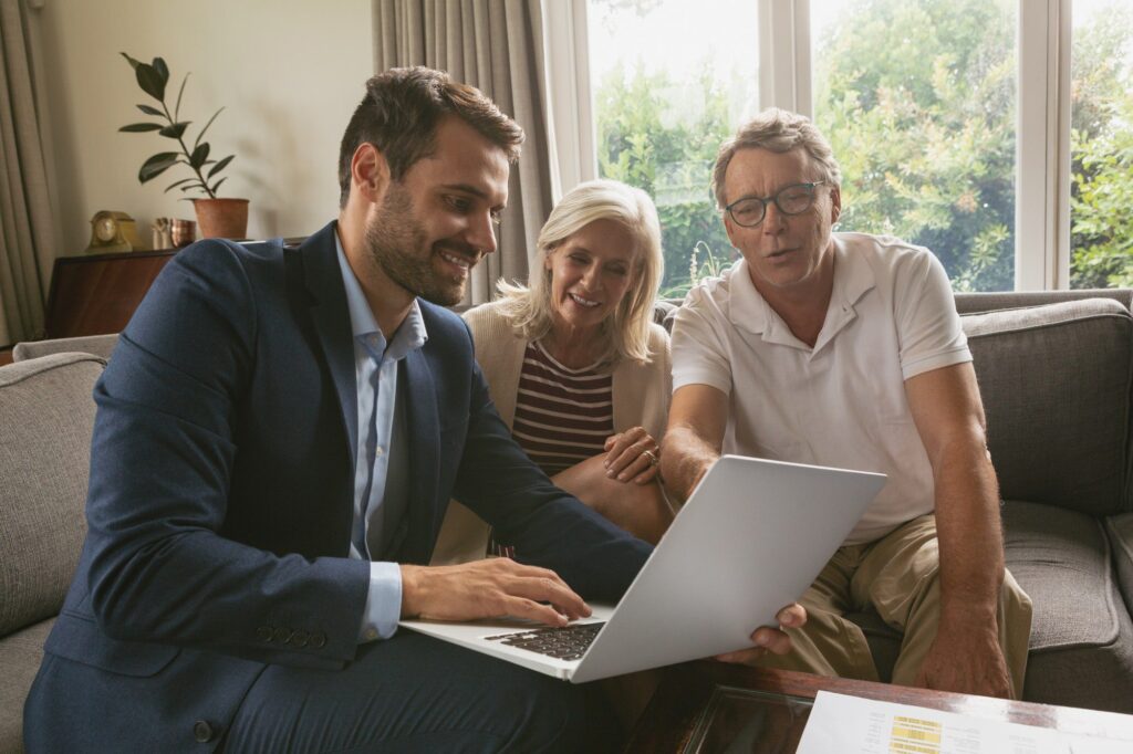 Active senior Caucasian couple discussing with real estate agent over laptop in living room at home going over Plan G Coverage, Cost, and Enrollment