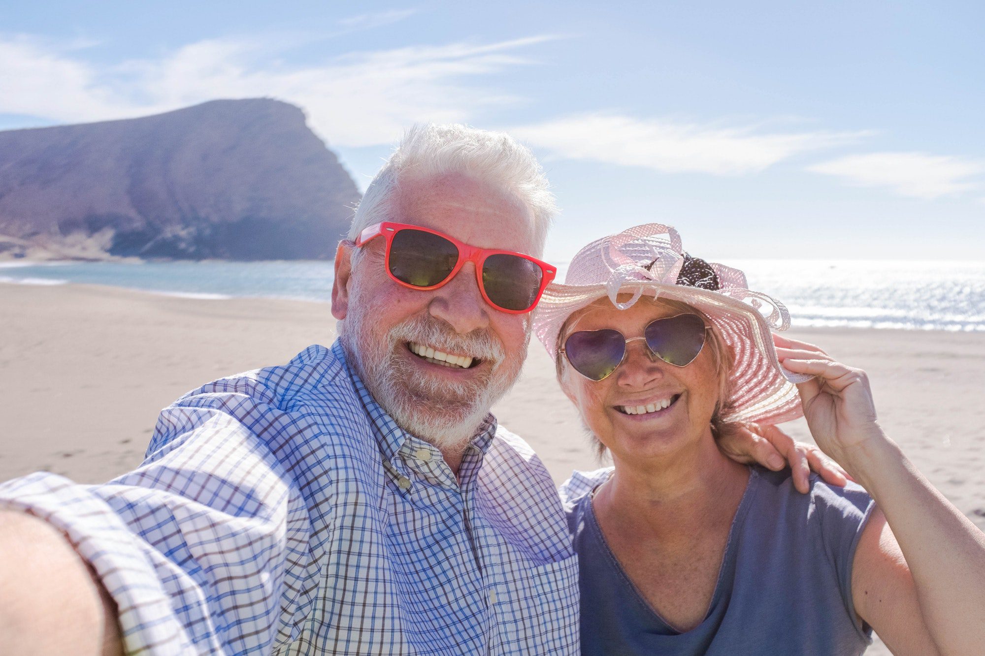 couple of seniors traveling and taking a selfie in a beautiful beach with a mountain knowing that their Medicare Supplement Plans work.