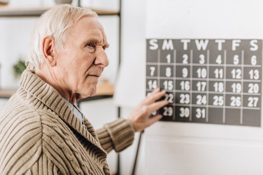 selective focus of senior man touching wall calendar checking Medicare Open Enrollment Period