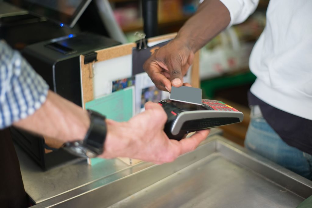 A customer taps a payment card on a card reader held by a shop assistant at a checkout counter.
