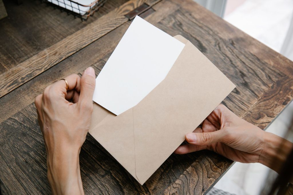 Two hands lift a folded letter out of a brown envelope on a wooden table.
