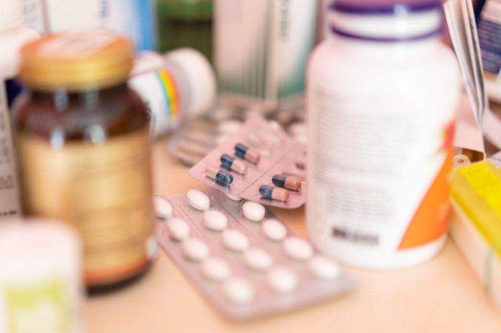 Assorted medication bottles and blister packs of tablets and capsules on a table.